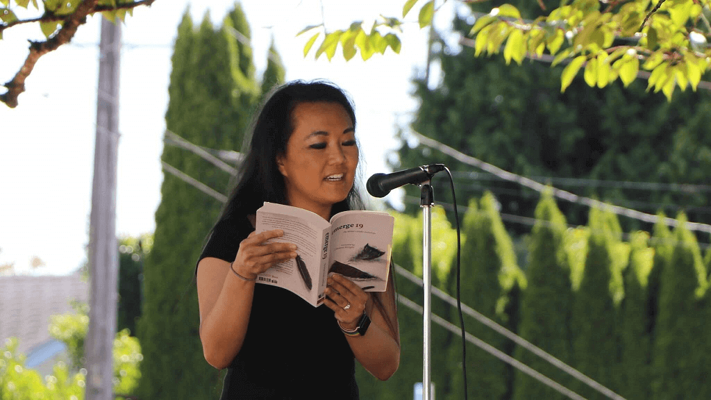 Me, reading outdoors at a microphone, from the anthology "emerge 19"